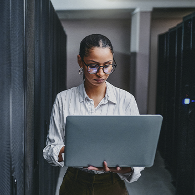 A woman works on a laptop in a server room