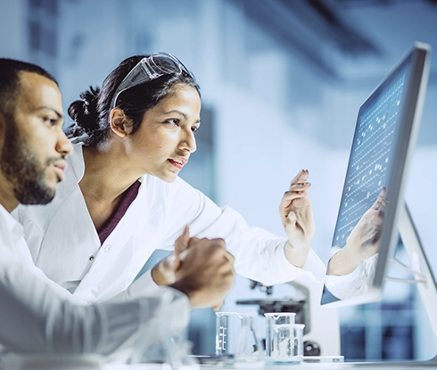 Two medical professionals wearing business attire look at a laptop