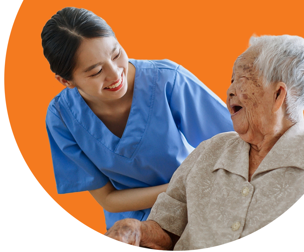 A medical professional wearing scrubs smiles at an elderly patient who is laughing.