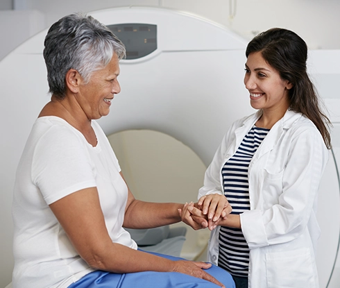 A medical professional wearing scrubs smiles at an elderly patient who is laughing.